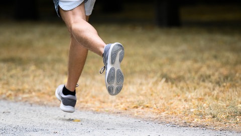 Ein Mann joggt im Sommer neben einer völlig vertrockneten Wiese. 