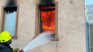Ein Mitarbeiter der Feuerwehr Worms hält einen Wasserschlauch in ein Fenster - die Wohnung steht in Flammen. 