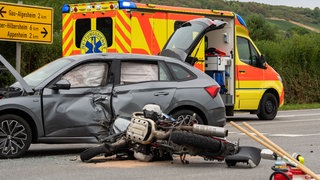 Ein Motorrad liegt zerstört vor einem zerbeulten Auto. Bei einem Unfall auf der L416 bei Gau-Algesheim ist ein Motorradfahrer schwer verletzt worden. 
