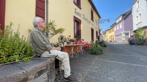 Ein Bewohner des Moselortes Kröv sitzt vor dem Teil des eingestürzten Hotels, der erhalten geblieben ist. Menschen haben dort Blumen niedergelegt und Kerzen angezündet, um ihrer Trauer Ausdruck zu verleihen.