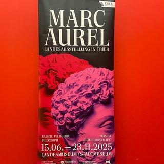 Das Ausstellungsplakat für die Landesausstellung zum römischen Kaiser Marc Aurel in Trier. Kaiserkopf in Rot und Pink.