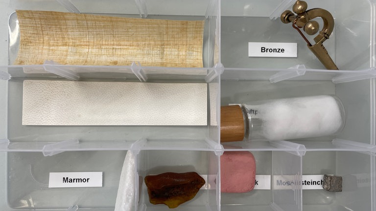 Box mit unterschiedlichen Materialien wie Bronze oder Papyrus zum Anfassen