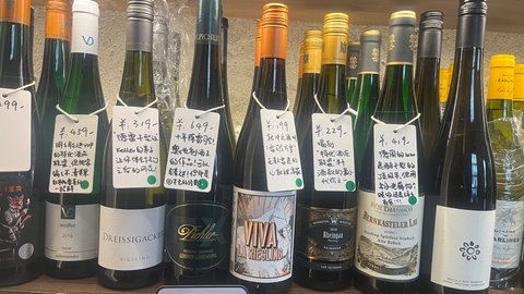 Liang Yang hat einige bekannte Weine von der Mosel im Angebot. Zusätzlich zu ihrem Orginaletikett haben die Weine ein weiteres Schild mit handschriftlichen chinesischen Schriftzeichen am Flaschenhals hängen. So wissen auch chinesische Kunden, was drin ist. 