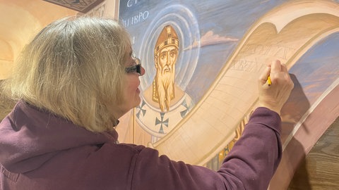 Ganz vorsichtig zeichnet die israelische Künstlerin kyrillische Buchstaben an die Wand der russisch-orthodoxen Kapelle in Klausen. 