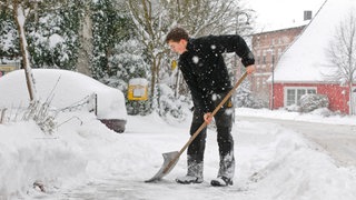 Ein Mann schippt den Schnee auf dem gehweg vor seiner Haustür auf Seite.