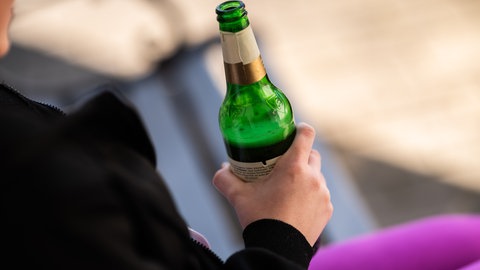 Eine Frau sitzt mit einer Flasche in der Hand da. Alkohol in der Schwangerschaft ist Gift für das ungeborene Kind.