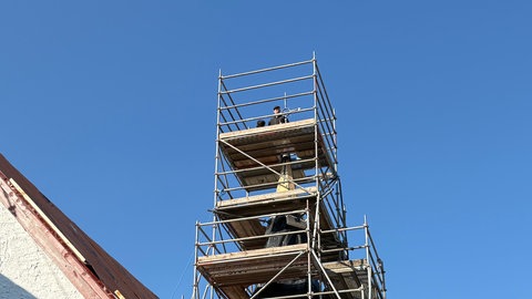 Auf der Baustelle in Naurath arbeiten mehrere Gewerke zusammen: Dachdecker, Maler, Zimmerleute und Kunstschmiede, die hier das Kreuz der Kirche wieder anbringen.