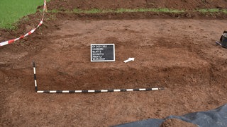 Bei einer kleinen Ausgrabung haben die Landesarchäologen genau hier einen alten Herd gefunden. Die Kohle konnten sie analysieren und damit zeitlich einordnen.
