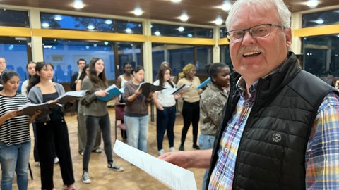 Werner Koch steht als Leiter vor den internationalen Mitgliedern des Chors im Cusanus-Studierendenwohnheim in Trier