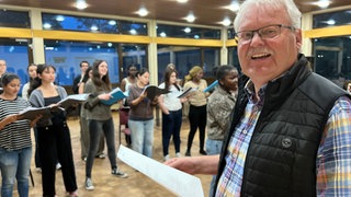 Werner Koch steht als Leiter vor den internationalen Mitgliedern des Chors im Cusanus-Studierendenwohnheim in Trier