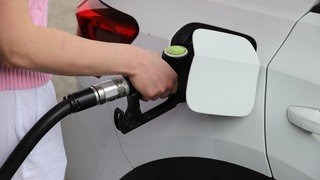 Frau steckt Zapfhahn in ihren Tank an einer Tankstelle