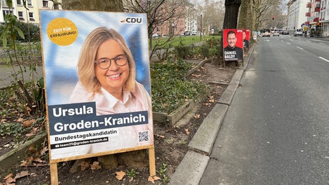 Ein Wahlplakat von Ursula Groden-Kranich an einem Baum in der Kaiserstraße in Mainz, an einem Baum dahinter ein Plakat von Daniel Baldy.