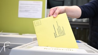 Ein Wahlbrief mit einem Stimmzettel für die Kommunalwahl wird im Rathaus in einem Wahllokal für die Briefwahl in eine Wahlurne gesteckt.