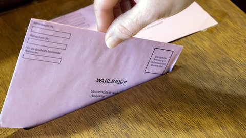 Eine Hand wirft einen Wahlbrief in die Wahlurne einer Gemeindeverwaltung - Symbolbild zur Landtagswahl RLP