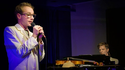 Schauspieler Carl Grübel bei Liederabend mit Pianist im Hintergrund