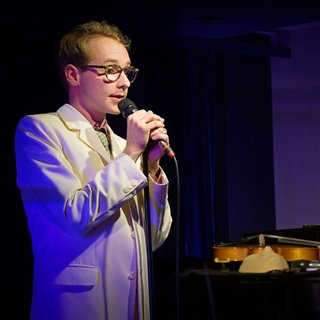 Schauspieler Carl Grübel bei Liederabend mit Pianist im Hintergrund