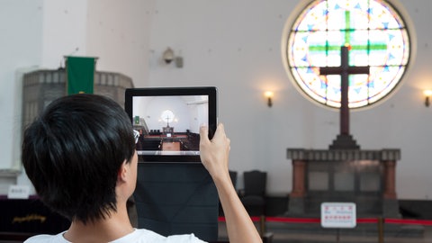 Ein Besucher fotografiert ein Kreuz und ein Kirchenfenster der evangelischen Kirche in Qingdao.