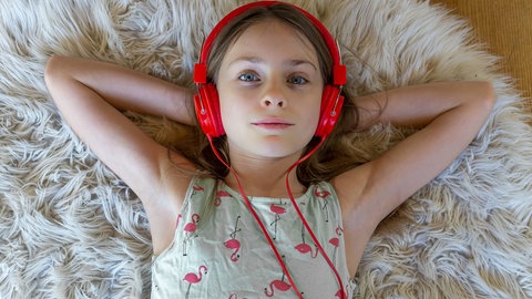 Ein Mädchen mit rotem Kopfhörern liegt auf dem Fußboden