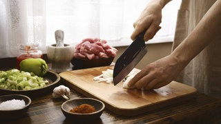 Fein Gemetzeltes - Ein Koch schneidet in einer Küche auf einem hölzernen Schneidebrett Zwiebeln in feine Streifen