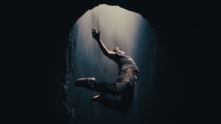 Person fällt durch eine dunkle Öffnung ins Licht.