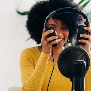 Eine Frau im gelben Pullover setzt sich Kopfhörer auf