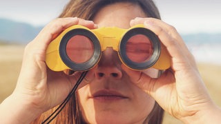 Podcast-Cover von "Das Wissen": Frau schaut durch Fernglas