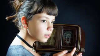 Mädchen hält ein altes Radio vor einem schwarzen Hintergrund 