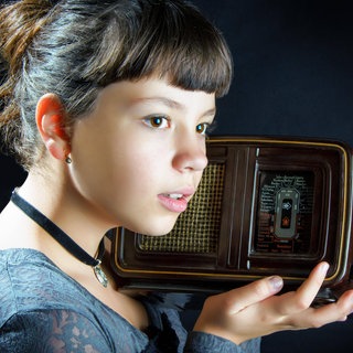 Mädchen hält ein altes Radio vor einem schwarzen Hintergrund 