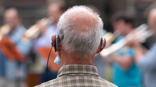 Ein Mann mit einer Hörprothese verfolgt ein Konzert von Blechbläsern