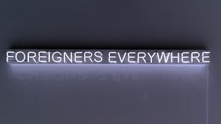 Leuchtende Schrift auf einer dunklen Wand: Foreigners Everywhere