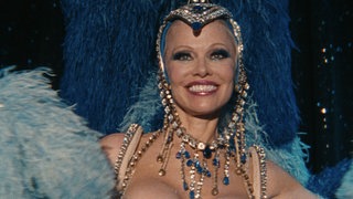 Pamela Anderson lächelt in einem Showgirl-Kostüm im Film „The Last Showgirl“
