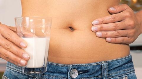 Frau mit einem Glas Milch hält sich die Hand auf den schmerzenden Bauch.