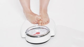 Eine Person steht verlegen auf einer Waage