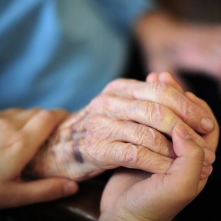 Eine junge Frau hält die Hand einer alten Dame: Heute ermöglichen rund 55.000 ehrenamtliche Helferinnen und Helfer eine ambulante Sterbebegleitung zu Hause. Doch junge Freiwillige, die sich engagieren wollen, fehlen.