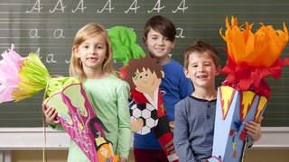 Drei Erstklässer stehen bei der Einschulung mit ihren Schultüten vor einer grünen Tafel