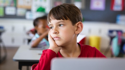 Ein Junge sitzt traurig in seiner Schulklasse und schaut abwesend in die Ferne. Zu oft werden Signale der Gewalt an Kindern nicht erkannt – auch nicht von jenen, die in Kitas, Schulen, Arztpraxen und Jugendämtern mit ihnen zu tun haben.