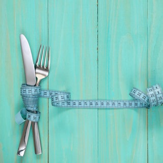 Besteck, umwickelt von einem Maßband (Symbolbild): “Bloß kein Gramm zu viel“: Lange dachte man, Ursache und Therapie von Magersucht liegen in der Familie. Doch neben der Psyche spielen auch Stoffwechsel und Genetik eine Rolle.