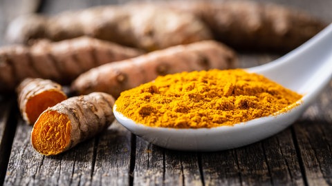 Kurkuma als Knolle und gemahlen auf einem Löffel