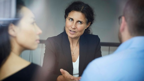 Eine Frau übernimmt die Rolle der Vermittlerin: Die unparteiische Mediatorin vermittelt im Streitgespräch. Dabei achtet sie darauf, dass alle gleichermaßen zu Wort kommen.