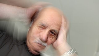 Ein älterer Mann fasst sich an seinen Kopf: Rund 30 Prozent aller Menschen in Deutschland erleben irgendwann in ihrem Leben Schwindel, auch Vertigo genannt, egal, wie alt sie sind. 