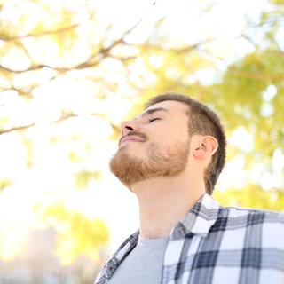 Ein Mann atmet entspannt im Park. Seitdem sich immer mehr Menschen für Achtsamkeit und Meditation interessieren, liegen Atem-Kurse, Atem-Apps und Ratgeber zum "richtigen Atmen" im Trend.