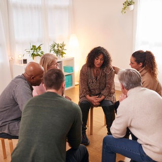 Menschen in einer Selbsthilfegruppe sitzen im Stuhlkreis und tauschen sich aus: Während die medizinische Fachwelt die Selbsthilfe lange skeptisch beäugte, wird sie heute als vierte Säule im Gesundheitswesen immer weiter gestärkt.