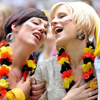 Zwei junge Frauen mit Blumenkette in Deutschland-Farben und der Hand auf dem Herzi singen beim Fußballspiel in Düsseldorf 2010 die Nationalhymne