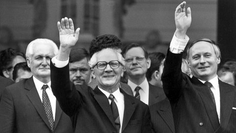 Geinsam winken der saarländische Ministerpräsident Oskar Lafontaine (rechts) und sein Gast, der DDR-Staatsratsvorsitzende und SED-Chef Erich Honecker (Mitte) nach der Besichtigung der barocken Ludwigskirche am 10.9.1987 in Saarbrücken den rund 100 Zuschauerrn zu. Links steht Honeckers Stellvertreter Günter Mittag.