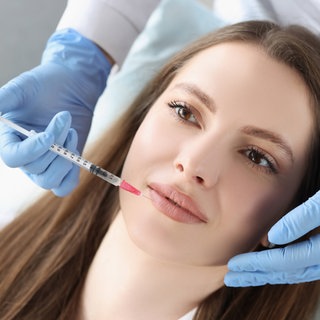 Junge Frau bekommt Injektion von Botox in ihre Lippen: Immer mehr junge Frauen lassen ihre Lippen aufpolstern, erste Fältchen straffen oder sich Implantate in den Po setzen. 