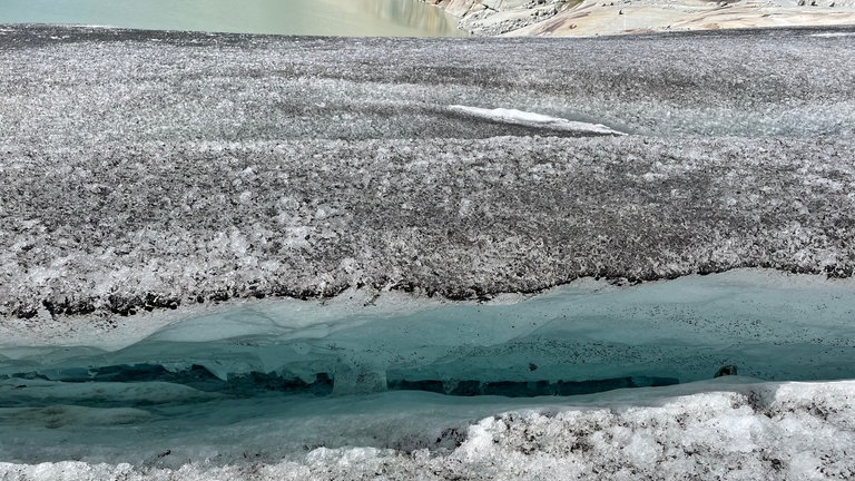 In der vermeintlich unberührten Natur der Alpen ist das Gletschereis oft schmutzig wie alter Schnee an einer Großstadtautobahn. Andreas Bauder: "Das Dunkle sind auch Rußpartikel [...] Die Rußpartikel, die sind natürlich von den menschlichen Emissionen, die wir in die Atmosphäre abgeben und die mit dem Niederschlag wieder auf die Oberfläche kommen." Die dunkle schmierige Schicht auf dem Gletscher bewirkt, dass das Eis umso schneller schmilzt. Der Gletscher hat Fieber. (Oktober 2022)