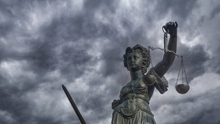Justitia am Gerechtigskeitsbrunnen am Römerberg in Frankfurt  Main vor dunklen Regenwolken: In Deutschland gibt es Fehlurteile. Die Hürden für die Wiederaufnahme eines abgeschlossenen Strafverfahrens sind jedoch sehr hoch gesetzt. 