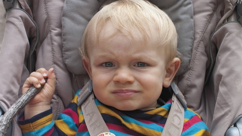 Kleiner Junge sitzt angeschnallt grantig im Buggy: Anschnallen – ob im Buggy oder im Kindersitz – dient der Sicherheit des Kindes. "Schützende Gewalt" ist dann etwas, was Eltern ggf. dem Kind gegenüber durchsetzen müssen, auch wenn es dem Kind in der Situation nicht gefällt.