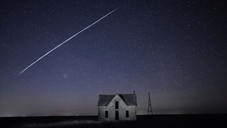 Auf diesem Foto, das am 6. Mai 2021 mit Langzeitbelichtung aufgenommen wurde, fliegt eine Reihe von Starlink-Satelliten über ein altes Steinhaus in der Nähe von Florence, Kansas