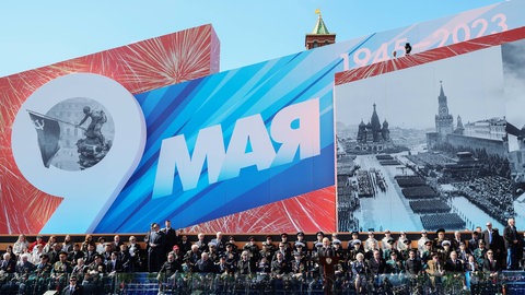 Wladimir Putin hält am "Tag der Befreiung", dem 9. Mai 2023, eine Rede in Moskau. Hinter ihm eine riesige Plakatwand, auf der u. a. zu lesen ist "1945 - 2023". Ganz links auf der Wand ist das ikonische Foto zu sehen, auf dem sowjetische Soldaten im Mai 1945 die rote Flagge auf dem Berliner Reichstag installieren und damit den Sieg über Nazi-Deutschland feiern. Im russischen Angriffskrieg gegen die Ukraine setzen beide Parteien immer wieder auf Propaganda – auch die Ukraine.